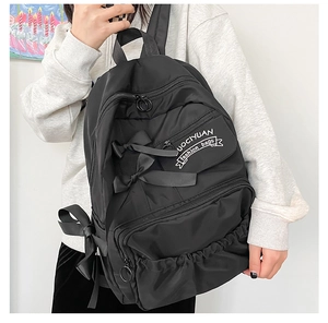 Detailansicht eines schwarzen Nylon-Rucksacks mit dekorativen Schleifen und Seitentasche