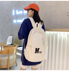 Detail view of cream canvas backpack with letter M print and cute bear keychain charm
