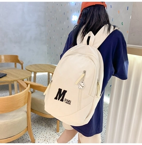 Detail view of cream canvas backpack with letter M print and cute bear keychain charm