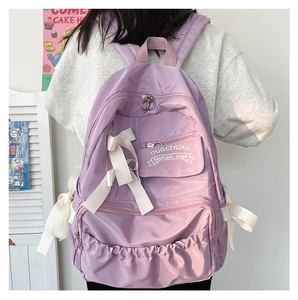 Detail eines lila Schulrucksacks mit weißen Seidenschleifen und mehreren Reißverschlussfächern