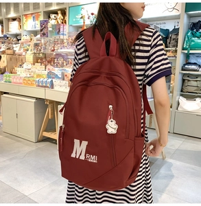 Detailed view of the burgundy waterproof nylon backpack featuring a white bear charm