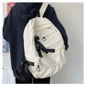 Detailansicht des cremefarbenen Rucksacks mit schwarzen Schleifen und Seitentaschen