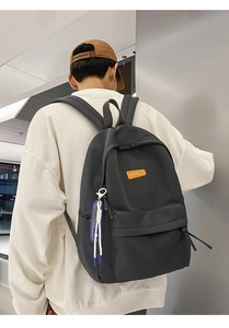 Rear view of a black casual backpack featuring an orange tag and a decorative cord pendant