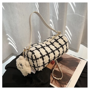 Close-up of black and white checkered tweed barrel bag with plush puppy charm detail