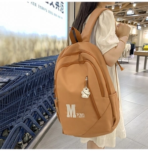 Close-up of khaki nylon backpack with white M RMI logo and cute bear pendant charm