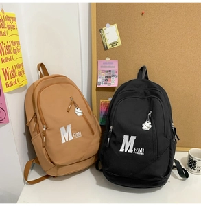 Detailed view of black and khaki student backpacks with cute bear charm and large M logo