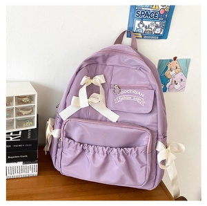 Detail eines lila Schulrucksacks mit Seidenschleifen auf einem Schreibtisch aus Holz