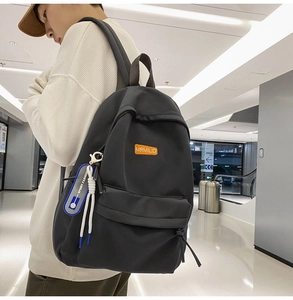 Side view of a black minimalist school backpack with orange logo and sporty pendant