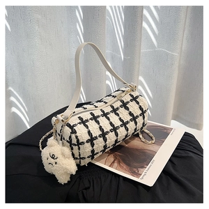 Close-up of black and white plaid tweed cylinder bag with white strap and plush charm