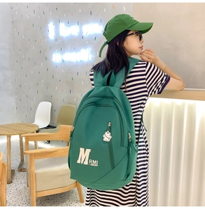 Detail of green nylon backpack with white bear keychain and matching baseball cap