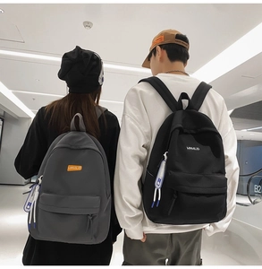 Two students wearing grey and black minimalist nylon backpacks in a modern corridor setting
