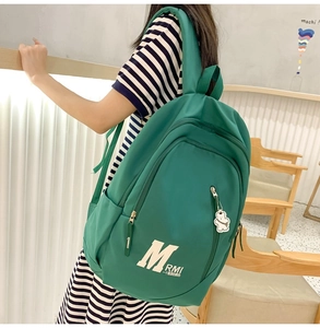 Detail of green nylon backpack showing metal zipper, bear charm, and printed text