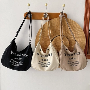 Three minimalist canvas crossbody bags in black and beige hanging on wooden wall hooks