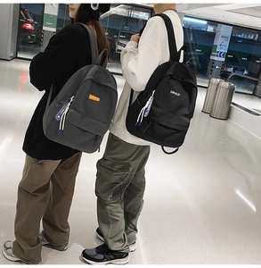 Side view of grey and black minimalist backpacks worn by models in a modern station