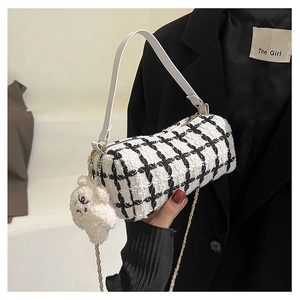 Detail of checkered tweed cylinder bag with white teddy bear charm and metal chain strap