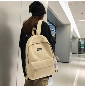 Detailed back view of a beige minimalist backpack worn by a model in a modern hallway