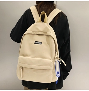 Close-up of a beige canvas backpack with a brand patch and blue decorative charm