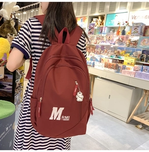Detailed back view of a burgundy nylon backpack with white bear charm for students