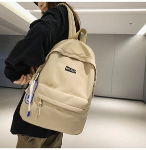 Detail view of the beige high-density nylon backpack showing front zip pocket and side strap