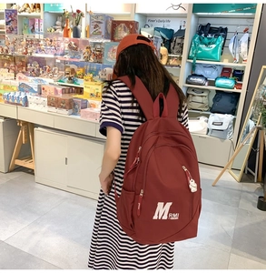 Detail view of burgundy vintage backpack showing water-resistant fabric and bear charm