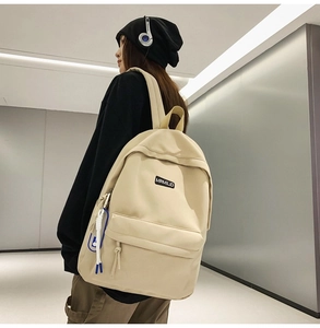 Detail view of a beige minimalist nylon backpack with side blue charm on a female model
