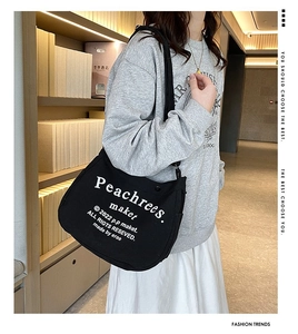 Lifestyle shot of large black canvas crossbody bag with white text on wooden background