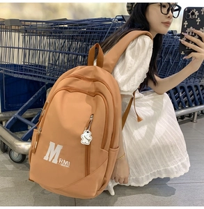 Detail of an orange-brown nylon backpack with side zip pockets and a cute bear pendant