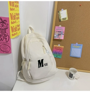Detailed view of white nylon backpack with multiple compartments and cute bear pendant