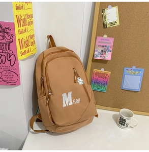 Close-up of khaki backpack with white bear pendant and letter M printed on canvas fabric