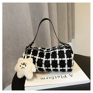 Close-up of black and white plaid tweed cylinder bag with white plush bear charm detail