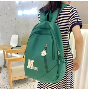 Close-up of green waterproof nylon backpack with letter printing and bear keychain detail