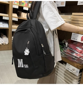 Close-up of minimalist black canvas backpack featuring letter prints and a bear charm