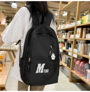 Close-up of black nylon backpack with letter print and a cute white bear keychain