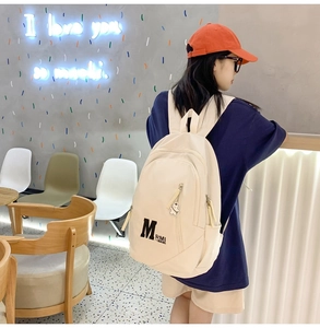Detail view of beige canvas backpack with bear pendant and adjustable side zipper