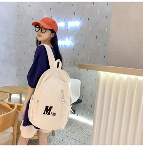 Detailed view of cream canvas backpack featuring multiple pockets and cute bear charm