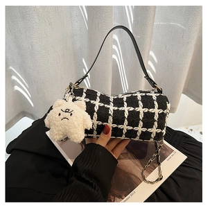 Detail of tweed checkered cylinder bag with plush bear charm and golden chain strap