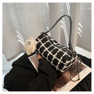 Detail of black and white checkered cylinder bag with plush bear charm and chain strap