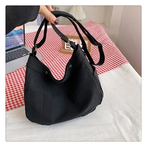 Detail of black canvas tote bag showing side pocket and adjustable wide shoulder strap