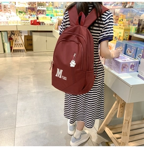 Detail view of burgundy vintage backpack with logo and white bear keychain pendant