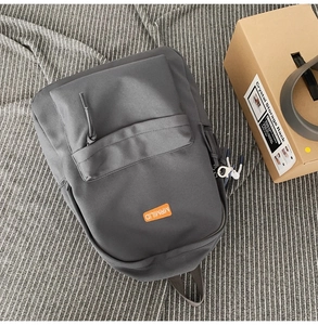 Close-up of dark grey backpack featuring a prominent orange brand label and durable zippers