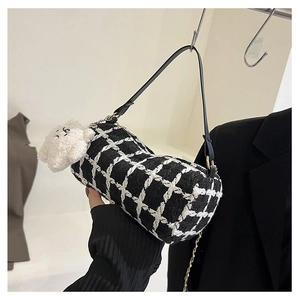 Detail of tweed checkered barrel bag with a fluffy white bear charm and metal chain strap