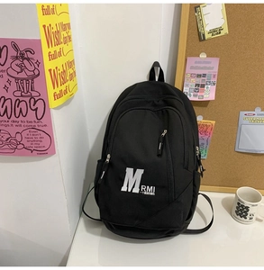Detailed close-up of a black canvas backpack featuring letter prints and diagonal zip pocket