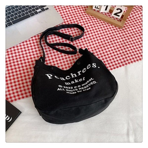 Detailed top view of black crescent canvas bag with white vintage text print and strap