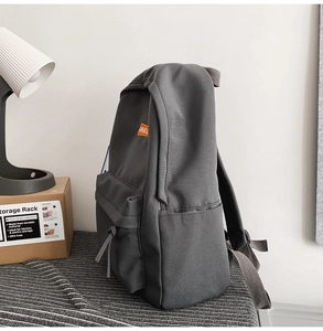 Detail of dark grey nylon backpack featuring orange logo patch and side pocket