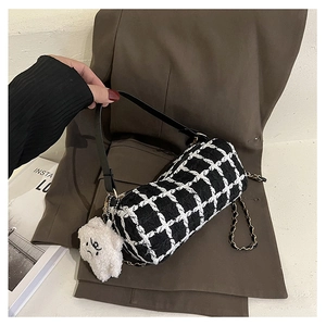 Close-up of black and white checkered cylinder bag with gold chain and plush bear charm