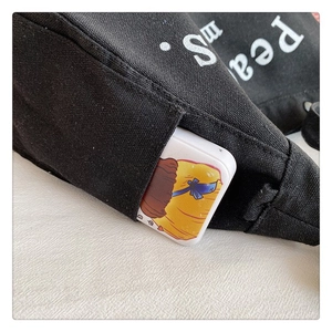Detail shot of the front pocket of a black canvas tote bag with a cartoon accessory
