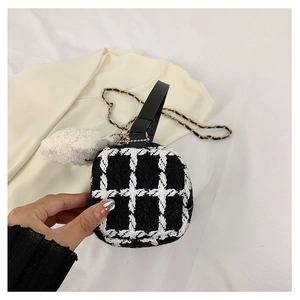 Detail of checkered tweed crossbody bag featuring black leather handle and plush pompom charm