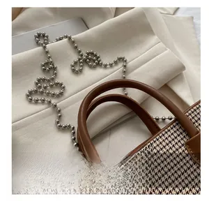 Detail of checkered houndstooth fabric handbag with premium leather handle and bead chain