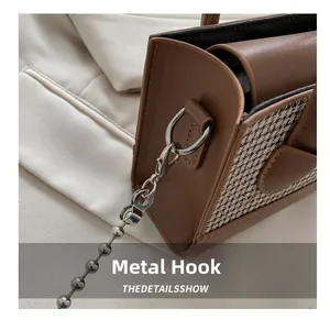 Detail of silver hardware hooks and bead chain on brown leather checkerboard bag