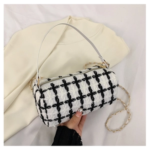 Close-up of black and white checkered tweed baguette bag with a gold chain and leather handle